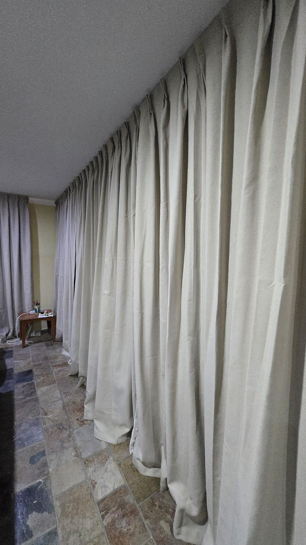 Floor-to-ceiling ivory wave-fold curtains, freshly installed and pooling gently at the floor